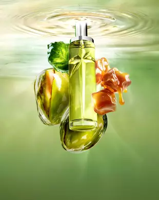 Nieuwe Starlicious Pistachio Praline stilleven met de slanke flacon, omringd door de belangrijkste ingrediënten: een patchouliblad, hele pistachenoten en druipende blokjes karamel, allemaal tegen een stralend groene achtergrond van kabbelend water.