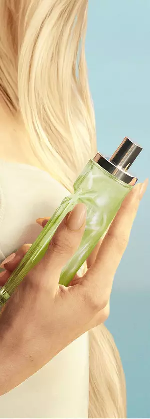 Nieuwe Starlicious Pistachio Praline in hand-asset met een model met lang blond haar en blauwe ogen, dat een lichtgele jurk draagt en de parfumflacon pistachio praline in de hand houdt